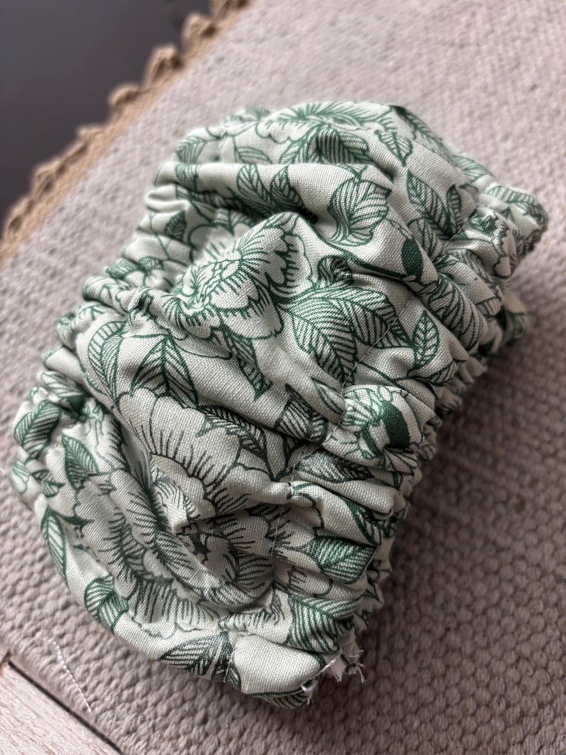 Puede incluir: Una tela floral verde y blanca con un dise&ntilde;o fruncido. La tela es suave y tiene un delicado estampado floral.