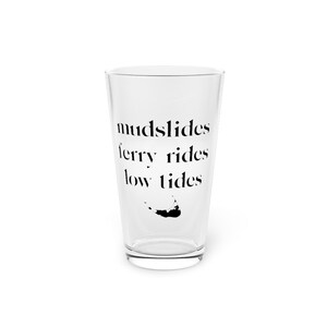 May include: A clear glass pint glass with the text "mudslides ferry rides low tides" and a black silhouette of an island.