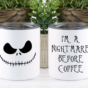 Może przedstawiać: Dwa białe ceramiczne kubki z czarnymi wzorami. Jeden kubek przedstawia twarz Jacka Skellingtona, drugi kubek ma napis "Jestem koszmarem przed kawą".