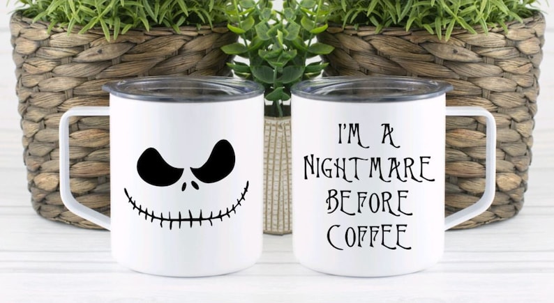 Może przedstawiać: Dwa białe ceramiczne kubki z czarnymi wzorami. Jeden kubek przedstawia twarz Jacka Skellingtona, drugi kubek ma napis "Jestem koszmarem przed kawą".