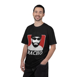 Może przedstawiać: Czarny t-shirt z grafiką brodatego mężczyzny w okularach przeciwsłonecznych i kapeluszu, na czerwonym tle. Słowo "MACHO" jest wydrukowane na dole na biało. T-shirt jest z krótkim rękawem.