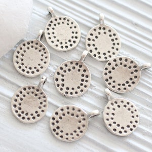 Peut inclure: Huit breloques rondes en m&eacute;tal argent&eacute; avec un motif circulaire d&eacute;coratif. Chaque breloque a une boucle pour l'attacher &agrave; un collier, un bracelet ou un autre bijou.