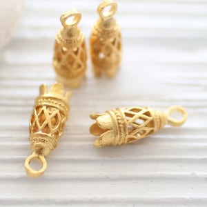 May include: Four gold-toned metal bead caps with intricate openwork designs. The caps have a cylindrical shape with a small loop at the top.