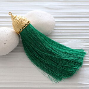 May include: A green tassel with a gold metal top. The tassel is made of soft, silky threads and has a decorative, ornate top.