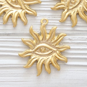 May include: Three gold-toned metal charms shaped like suns with an eye in the center. Each charm has a loop at the top for attaching to a necklace or bracelet.