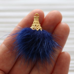 May include: A blue faux fur pom pom with a gold metal top. The top has a decorative design and a loop for attaching.