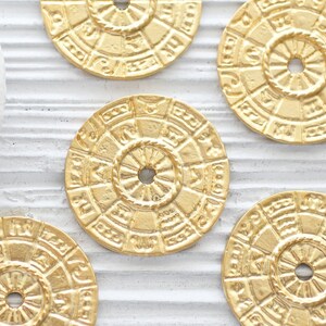 Pu&ograve; includere: Cinque ciondoli rotondi in metallo color oro con disegni intricati. Ogni ciondolo presenta un motivo circolare con un foro centrale. I ciondoli hanno un bordo leggermente rialzato e una superficie testurizzata.