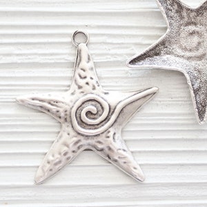May include: Two silver starfish charms with a swirl design on one. The charms have a loop at the top for attaching to jewelry.