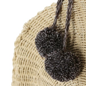 May include: A beige woven straw bag with two brown and white pom-poms attached to the handles.