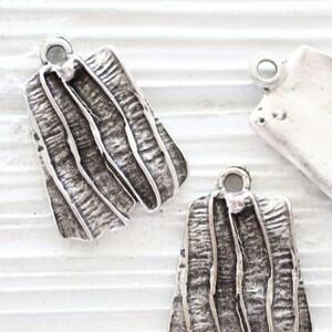 May include: Three silver charms with a textured, organic design. Two charms feature a vertical, striped pattern, and one charm is smooth and blank.