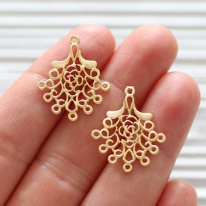 May include: Two gold filigree metal charms with a floral design. The charms have a loop at the top for attaching to jewelry or other crafts.