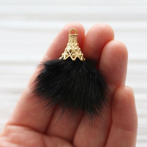 May include: A black faux fur pom pom with a gold metal top. The top has a decorative design with small beads.