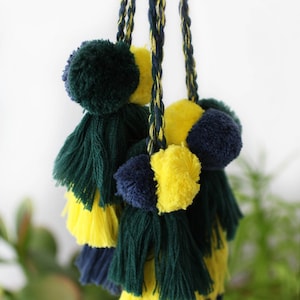 Könnte beinhalten: Ein Satz bunter Quasten mit grünen, gelben und blauen Bommeln. Die Quasten sind aus Garn gefertigt und hängen an einer Schnur.