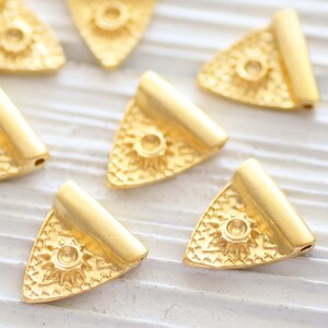 May include: Six gold-toned triangle-shaped metal charms with a sun design in the centre. The charms have a flat back and a small hole at the top for attaching to jewellery or other crafts.