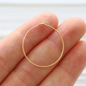 May include: A pair of gold hoop earrings. The hoops are thin and delicate, and they are held together by a small clasp.