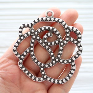May include: Silver metal rose charm with a delicate, intricate design. The rose is made of small, round beads that are connected to form a floral pattern.
