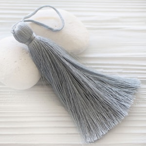 May include: A light gray tassel with a loop for hanging. The tassel is made of soft, silky fibers and is approximately 10 inches long.