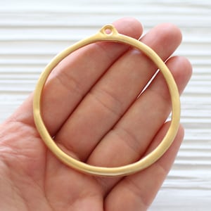 May include: A gold-colored metal circle with a small hole at the top. The circle is about 2 inches in diameter.