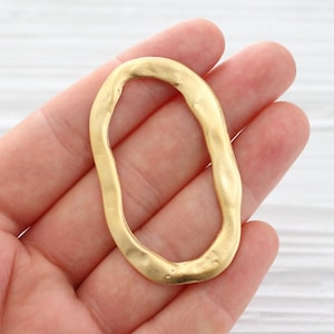 May include: Gold-toned metal oval ring with an irregular, slightly wavy edge. The ring is about 2 inches in diameter.