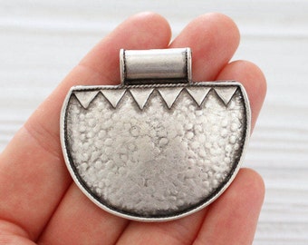 May include: Silver pendant with a half-circle shape and a textured surface. The pendant has a decorative border with a repeating triangle pattern.