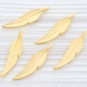 May include: Five gold-colored metal feather charms. The feathers are all the same size and shape, with a slightly textured surface.