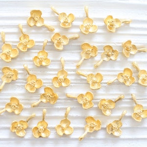 May include: A collection of gold-toned metal flower charms with a loop for attaching to jewelry or other crafts.
