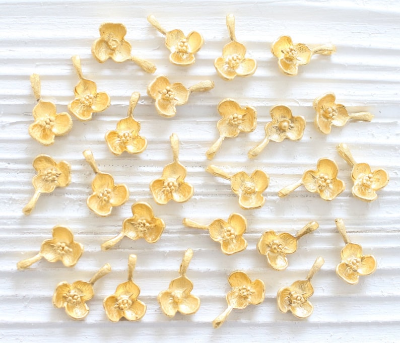 May include: A collection of gold-toned metal flower charms with a loop for attaching to jewelry or other crafts.
