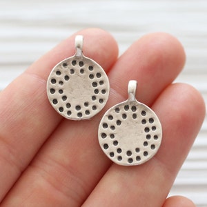 Peut inclure: Deux breloques pendantes en m&eacute;tal argent&eacute; de forme circulaire. Chaque breloque a un cercle de petits trous autour du bord.