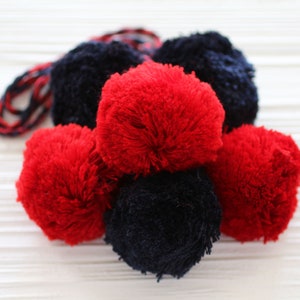 Puede incluir: Un grupo de pompones rojos y negros esponjosos. Los pompones están atados juntos con una cuerda.