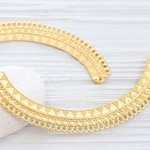 May include: Two gold metal decorative trim pieces with a geometric pattern. The trim pieces are curved and have a scalloped edge.