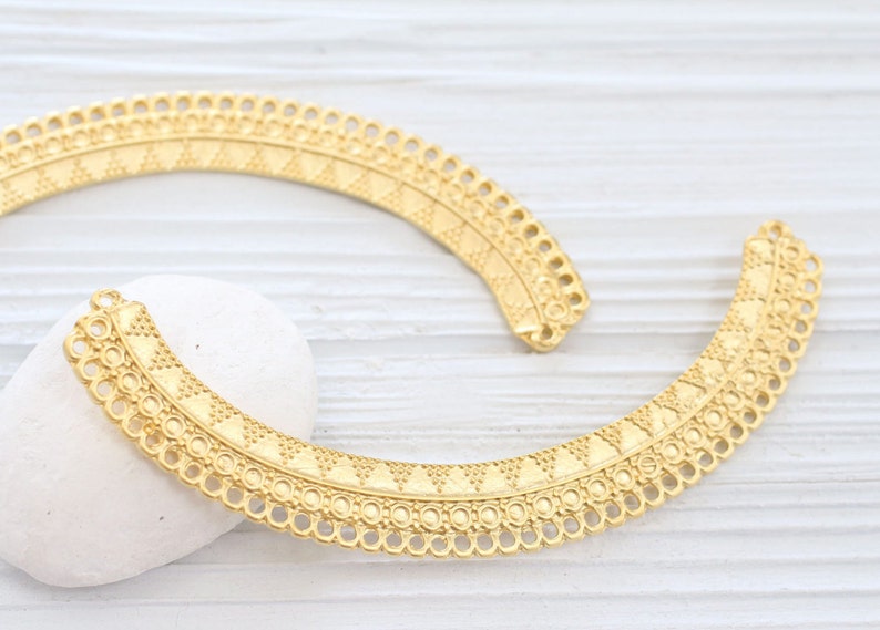 May include: Two gold metal decorative trim pieces with a geometric pattern. The trim pieces are curved and have a scalloped edge.