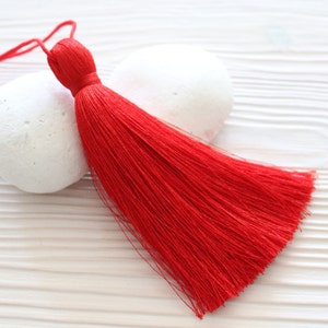May include: A bright red tassel with a long, flowing fringe. The tassel is made of soft, silky threads and has a small, knotted top.