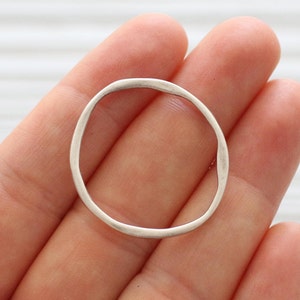 May include: A silver, irregularly shaped, open circle pendant.