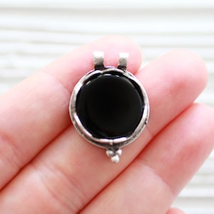 May include: A silver pendant with a black onyx stone in a round setting. The pendant has a bail for attaching to a chain.