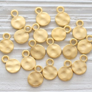 May include: A collection of 15 gold-toned metal circle charms with a loop at the top. The charms have a hammered texture.