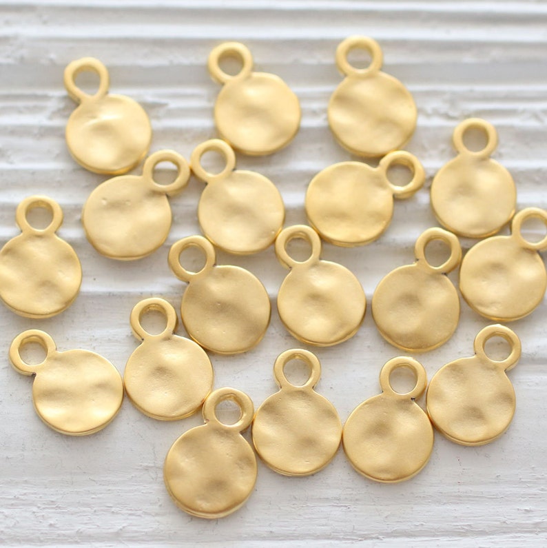 May include: A collection of 15 gold-toned metal circle charms with a loop at the top. The charms have a hammered texture.