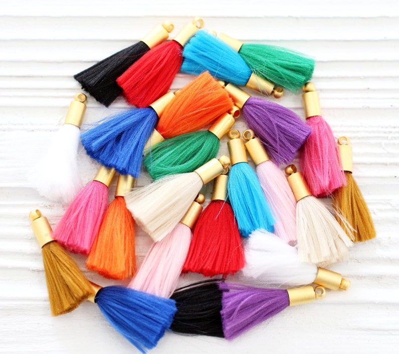 May include: A collection of colorful tassels with gold metal caps. The tassels are made of soft, fluffy fibers and come in a variety of colors, including red, blue, green, pink, orange, white, and black.