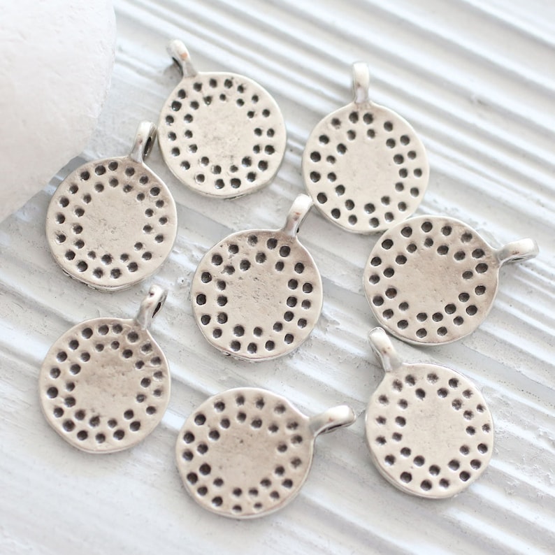 Peut inclure: Huit breloques rondes en m&eacute;tal argent&eacute; avec un motif circulaire d&eacute;coratif. Chaque breloque a une boucle pour l'attacher &agrave; un collier, un bracelet ou un autre bijou.