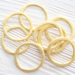 May include: A set of six gold-colored metal rings of varying sizes. The rings are arranged in a circular pattern on a white wooden surface.