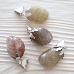 May include: Three silver pendants with different colored stones. The stones are all oval shaped and have a natural, rough texture. The pendants are attached to silver chains.