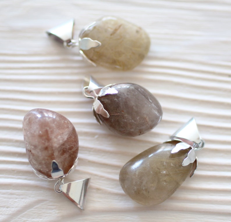 May include: Three silver pendants with different colored stones. The stones are all oval shaped and have a natural, rough texture. The pendants are attached to silver chains.