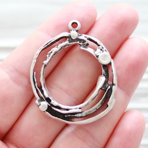 May include: Silver pendant with a circular design featuring a textured, swirling pattern. The pendant has a loop at the top for attaching a chain.