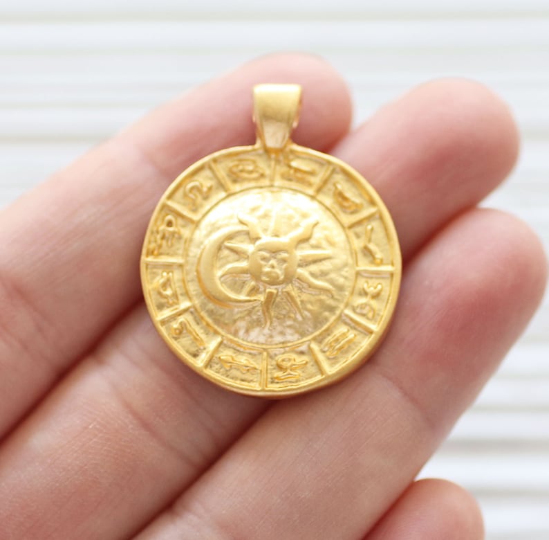 Puede incluir: Colgante dorado con un dise&ntilde;o circular con los s&iacute;mbolos del zod&iacute;aco y un gr&aacute;fico de sol y luna.