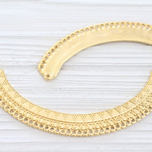 May include: Two gold metal decorative trim pieces with intricate designs. The trim pieces are shaped like half circles and have a scalloped edge.