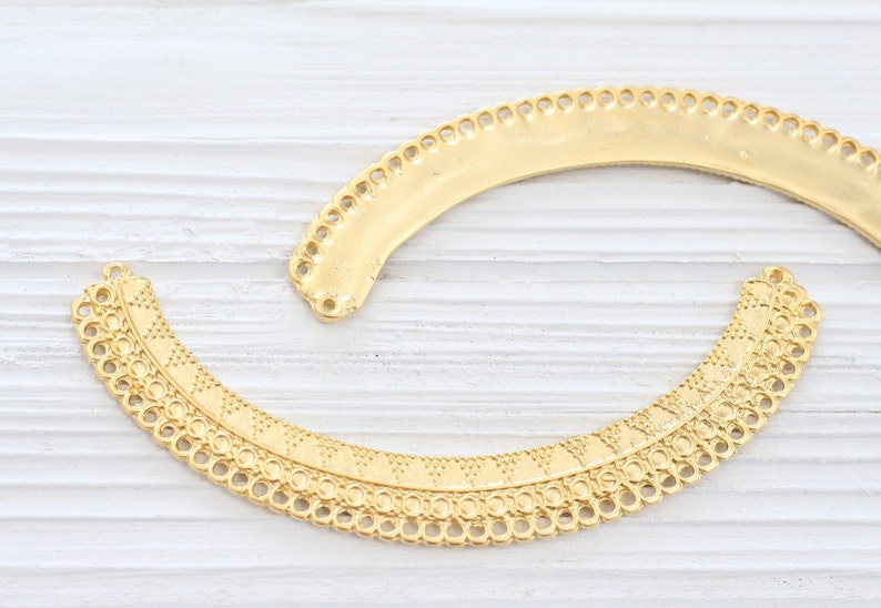 May include: Two gold metal decorative trim pieces with intricate designs. The trim pieces are shaped like half circles and have a scalloped edge.