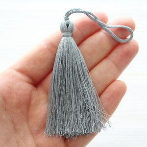May include: A gray tassel with a loop at the top. The tassel is made of soft, silky threads.