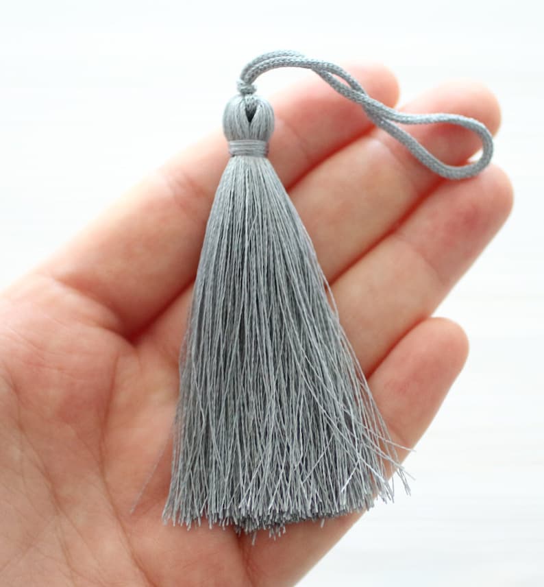May include: A gray tassel with a loop at the top. The tassel is made of soft, silky threads.