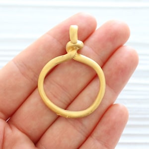 Peut inclure: Pendentif en m&eacute;tal dor&eacute; avec un design de n&oelig;ud torsad&eacute; formant un cercle. Le pendentif est lisse et a une finition mate.