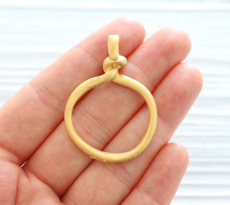 Peut inclure: Pendentif en m&eacute;tal dor&eacute; avec un design de n&oelig;ud torsad&eacute; formant un cercle. Le pendentif est lisse et a une finition mate.
