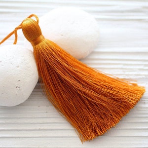 May include: A bright orange tassel with a long, flowing fringe. The tassel is made of soft, silky material and has a simple, elegant design.